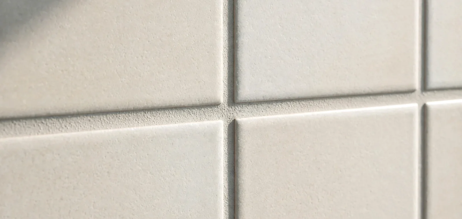 Zbliżenie na jasne, kwadratowe płytki ceramiczne z równo wypełnionymi, szarymi spoinami.